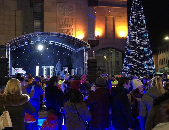 Persons gathered around the stage and Christmas tree