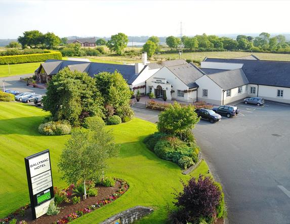 Image shows hotel and grounds with grass area and sign re hotel name. Also shows parking areas