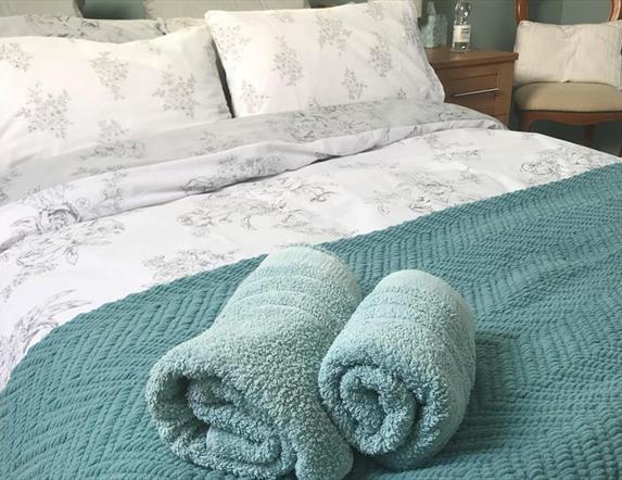 Image shows double bed with rolled up towels at the bottom