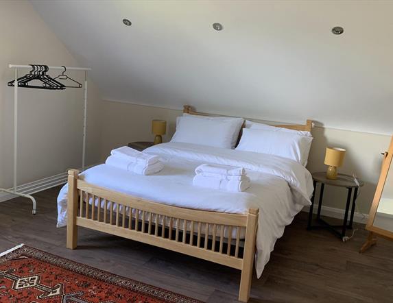 Image shows bedroom in loft with double bed, dressing mirror and clothes rail