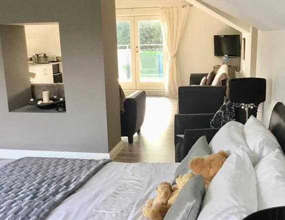 Image shows double bed with teddy bears and sitting area with patio doors to outside