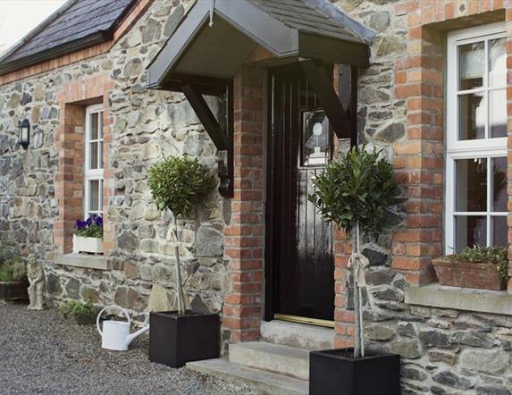 Image shows outside of stone property with bay tree plants at either side of front door