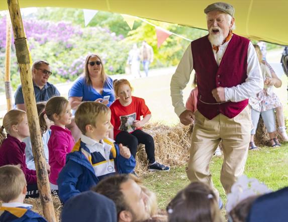 Image shows man in a purple waist coat with cap dancing with a group of children looking on