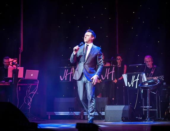 Image is of singer James Huish performing on stage