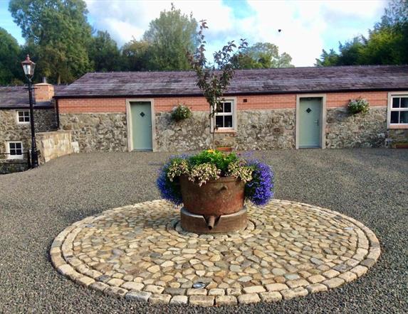 Image shows front of cottages with flower bed in a stone circle