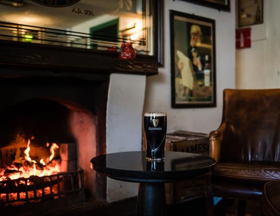 Image is of open fire and pint of Guinness on table in The Hillside Bar in Royal Hillsborough