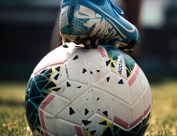 An image of a football with someone holding it in place by their football boot