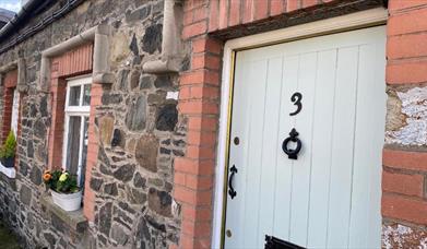 Image shows front door of property with flower beds on window sills