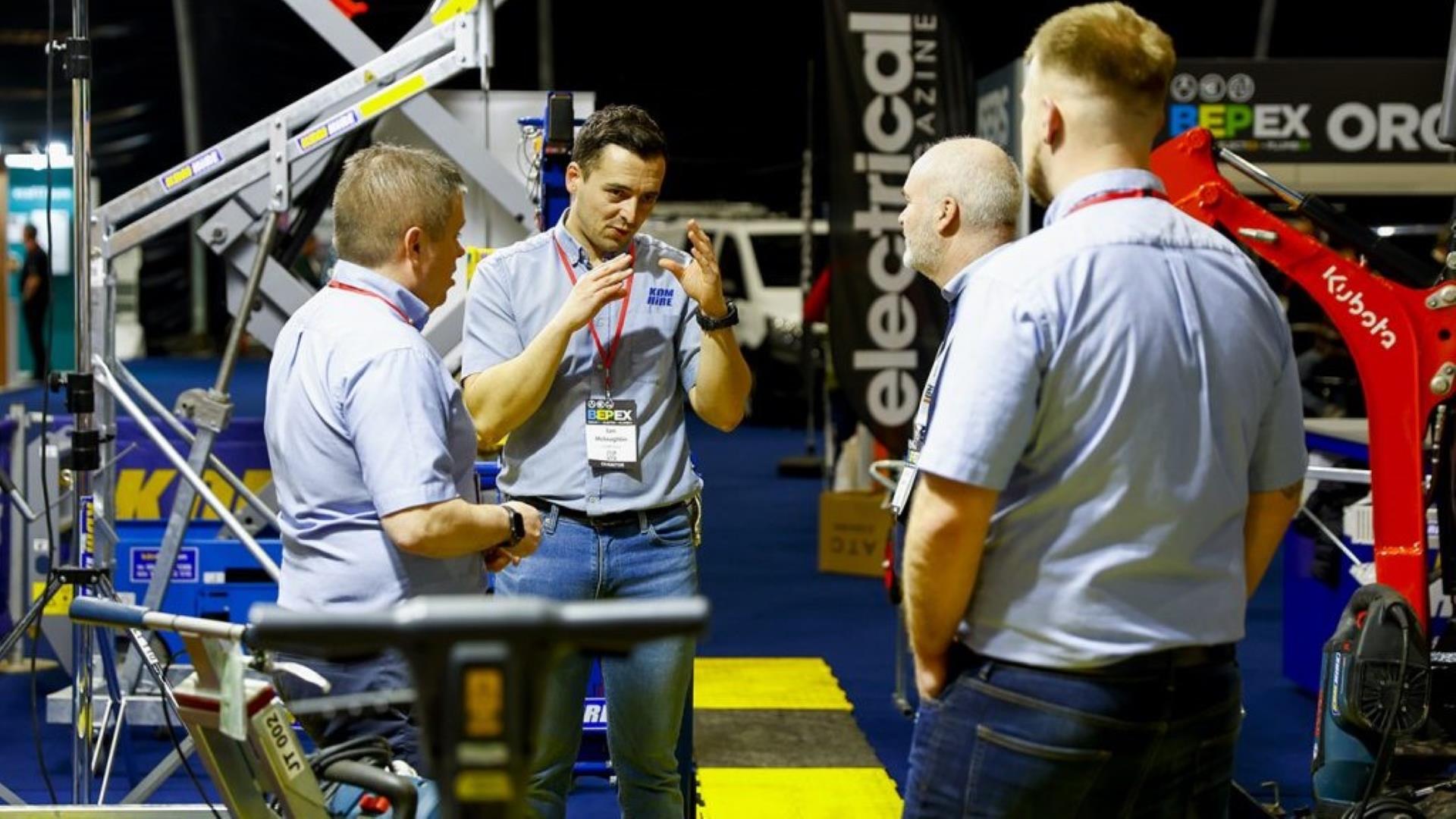 Image shows 4 men standing chatting at a trade show, with machinery & trade equipment in the background.