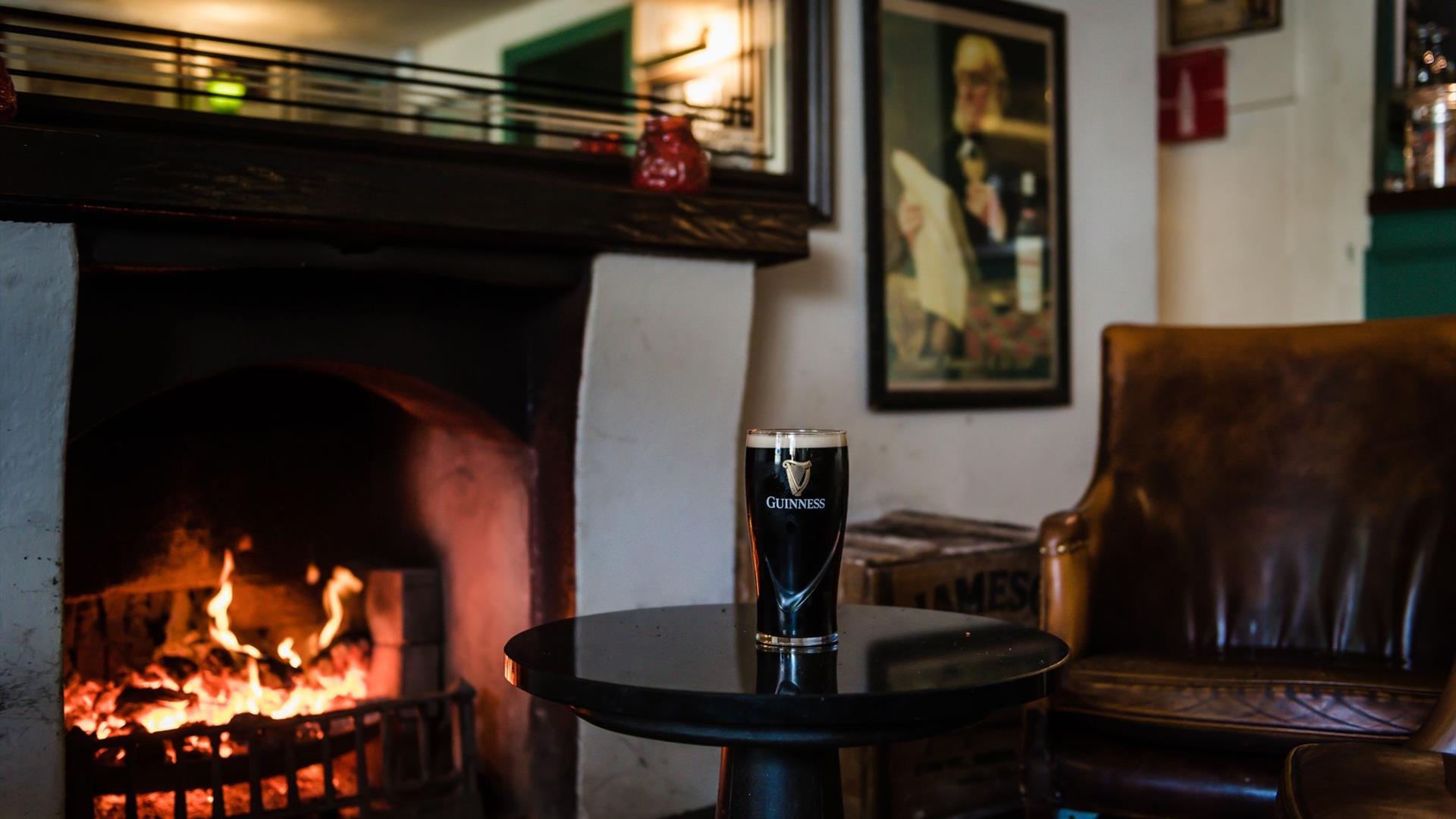 Image is of open fire and pint of Guinness on table in The Hillside Bar in Royal Hillsborough