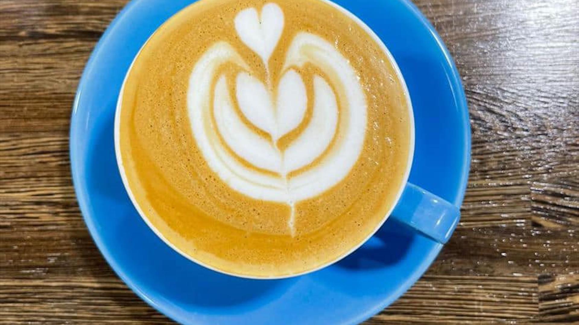 Image shows a blue coffee cup and saucer with a beautifully decorated latte coffee