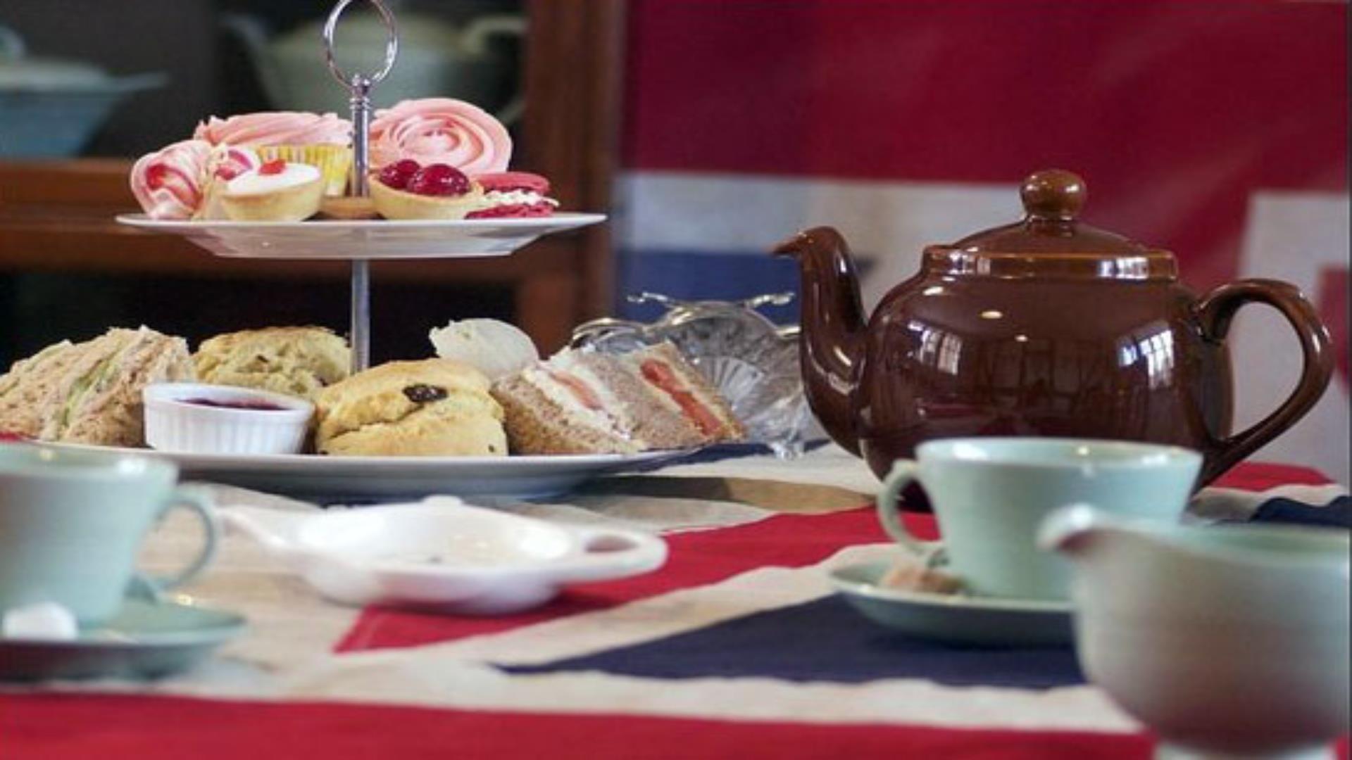 Image shows a tea set with cakes and sandwiches.