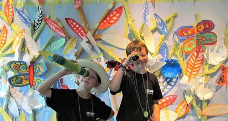 Two children looking through binoculars with art on the walls behind them