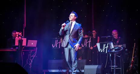 Image is of singer James Huish performing on stage