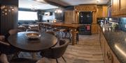 Image shows kitchen/dining area with round table & high table, with Large Settee in background, TV on wall