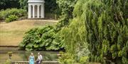 A couple sit by the lake at Hillsborough Castle and Gardens, with Lady Alice's Temple in the background