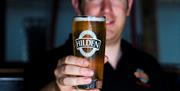 Image shows a smiling bartender holding a pint of Hilden beer