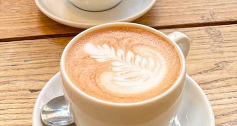 Image shows two white cups with latte coffees