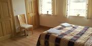 Image shows double bedroom with chair, 2 windows and door to ensuite