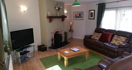 Image shows lounge area with leather sofas, fireplace, coffee table and TV