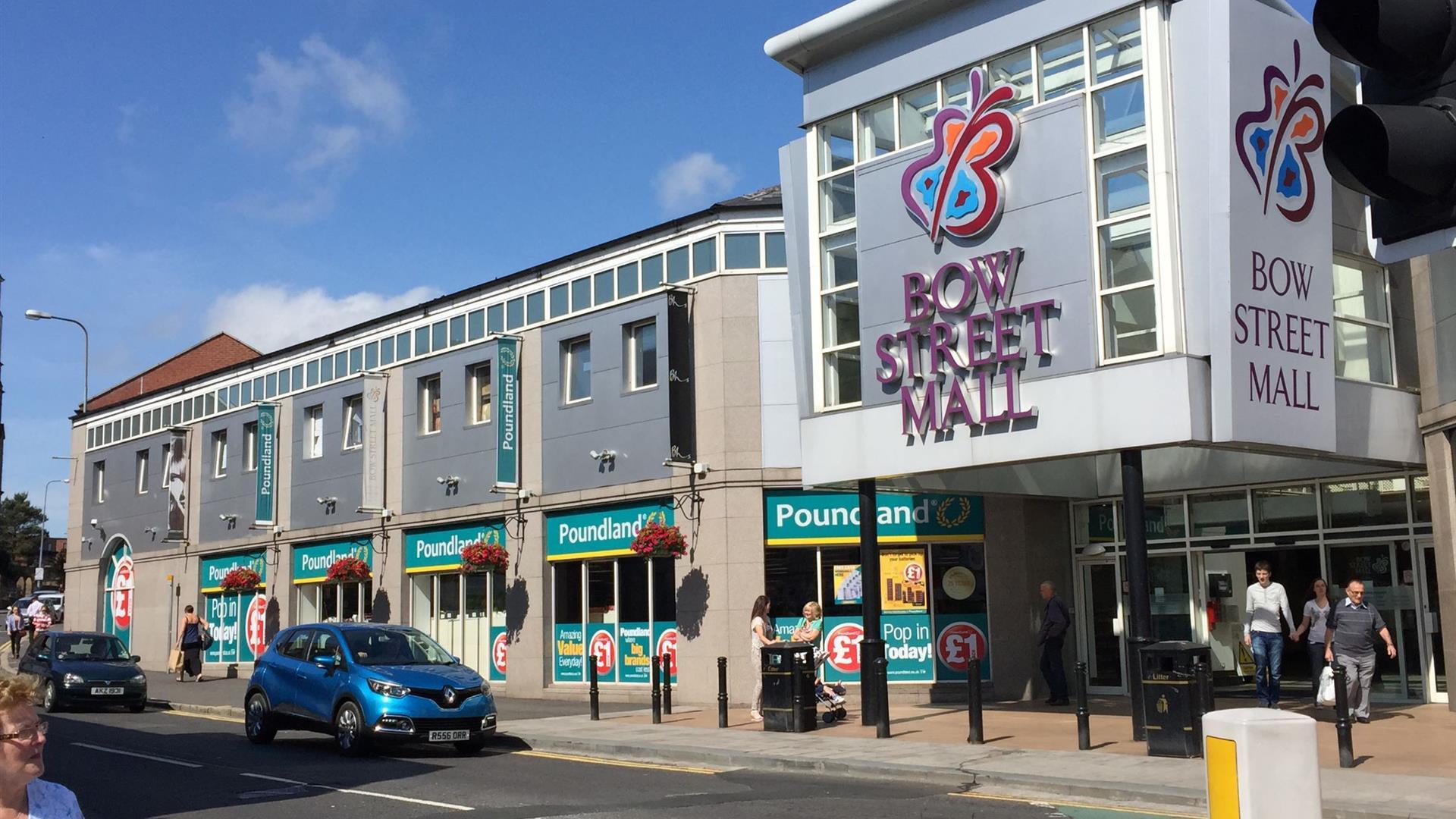 Image shows entrance to Bow Street Mall with visitors exiting the mall and cars driving by Image shows entrance to Bow Street Mall with visitors exiting the mall and cars driving by