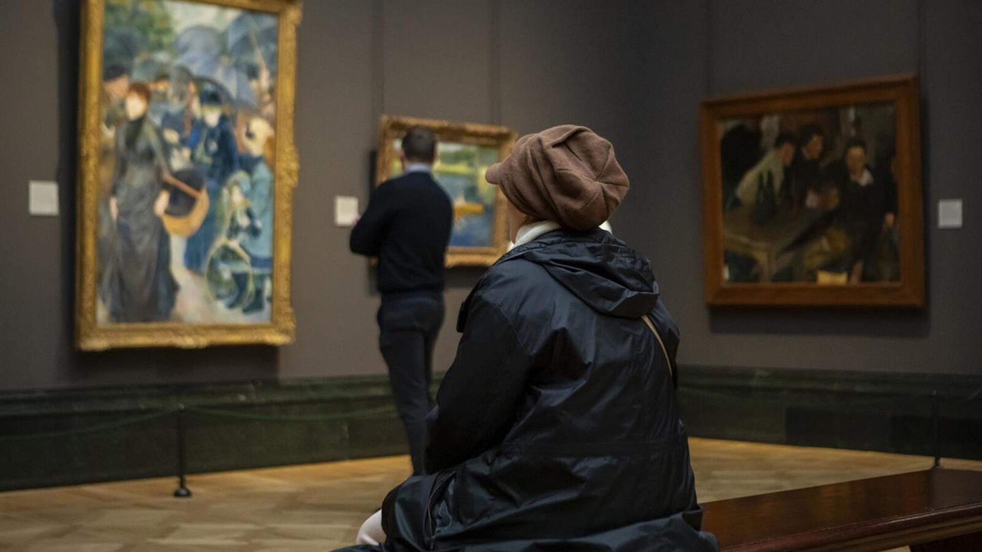 Picture of 2 people looking at works of art, one is sitting and one is standing