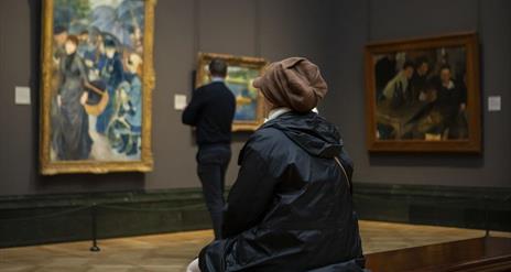 Picture of 2 people looking at works of art, one is sitting and one is standing